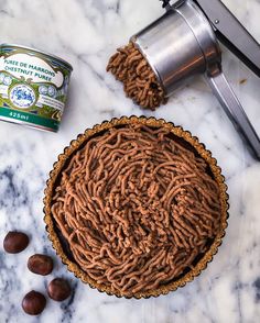 a chocolate pie next to a can of almonds on a marble counter top with a grinder