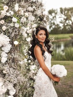 a beautiful woman in a white dress standing next to a flower covered arch with flowers