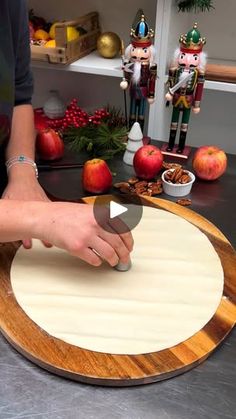 a person cutting up food on top of a wooden board with an apple in the background