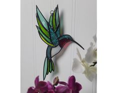 a glass hummingbird hanging on the side of a door with purple flowers in front of it