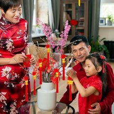 a man, woman and child are decorating a vase with red flowers on it