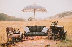 a couch, chair and umbrella sitting in the middle of a field with tall grass