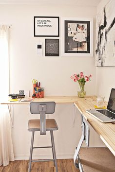 a desk with a laptop computer on top of it next to a chair and flowers