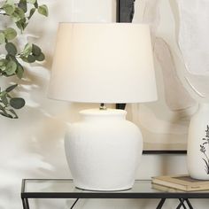 a white vase sitting on top of a table next to a lamp