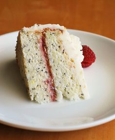 a piece of cake with white frosting and raspberries sits on a plate