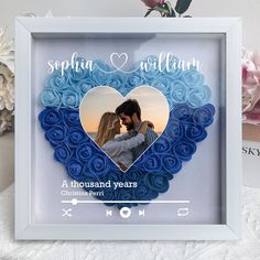 a blue heart shaped photo frame with a couple in the center and flowers behind it