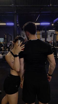 a man and woman standing in a gym looking at their cell phones