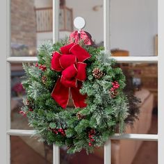 a christmas wreath hanging on a window sill with pine cones and red berries in the center