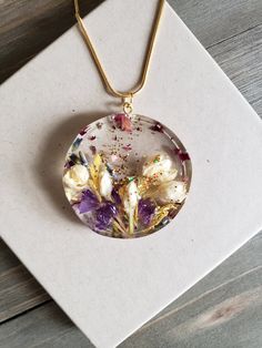 a necklace that has flowers inside of it on a white card with a gold chain