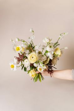 a person holding a bouquet of flowers in their hand on a beige background with white and yellow colors