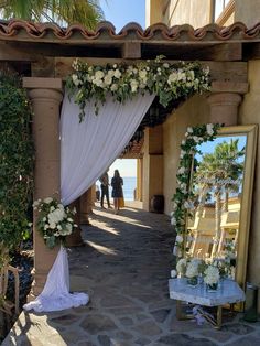 an outdoor wedding setup with white flowers and greenery on the arch, near a large mirror