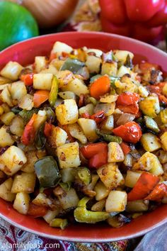 a red bowl filled with cooked vegetables on top of a table next to green peppers