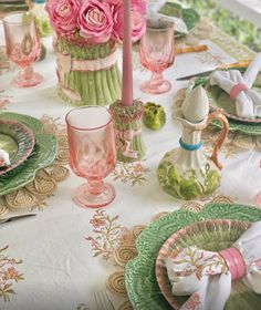 the table is set with pink roses and green dishes, napkins, and plates