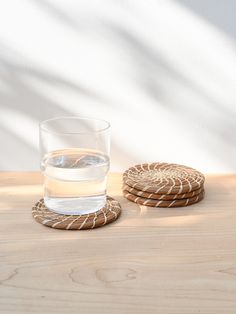 a glass of water sitting on top of a wooden table next to two coasters