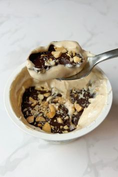 an ice cream sundae with chocolate and nuts in a white bowl on a marble table