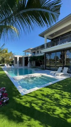 an empty swimming pool in front of a large house with lawn and palm trees on the side