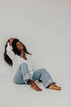 a woman sitting on the floor with her arms behind her head, smiling and looking up