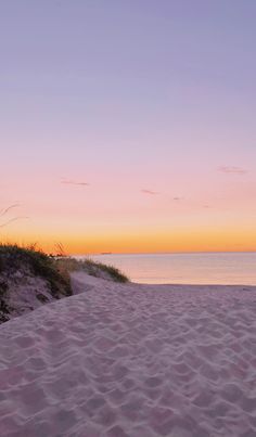 the sun is setting at the beach and there are sand dunes in front of the water