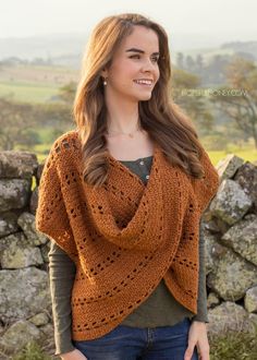 a woman wearing an orange crochet shawl standing in front of a stone wall