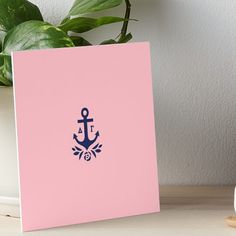 a pink card with an anchor on it next to a potted plant and white vase