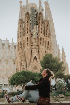 a woman sitting on the ground in front of a building with many spires and windows