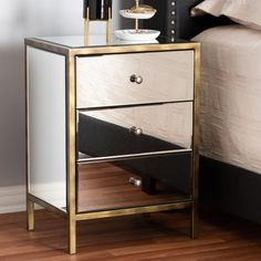 a nightstand with two drawers on top of it next to a white and gold bed