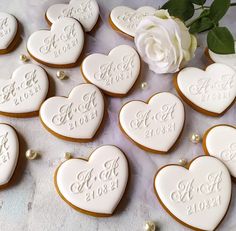 wedding cookies with names and date on them next to a white rose, in the shape of hearts