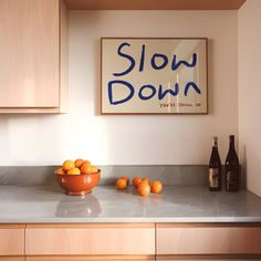 a bowl of oranges sitting on top of a counter next to bottles and a sign that says slow down