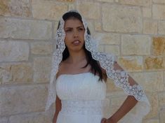 a woman in a white wedding dress with a veil on her head standing next to a brick wall