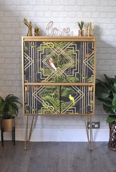 an ornate chest of drawers with birds and plants on it in front of a brick wall