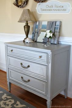 a gray dresser with two pictures on top and a lamp next to it in the corner