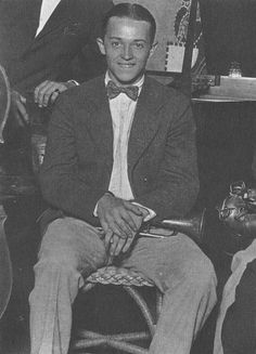 a man in a suit and bow tie sitting on a chair