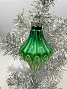 a green glass ornament hanging from a silver christmas tree