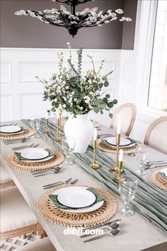 a dining room table with place settings and flowers in a vase on the centerpiece