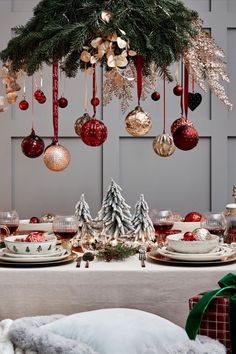 a dining room table decorated for christmas with ornaments hanging from the ceiling and plates on it