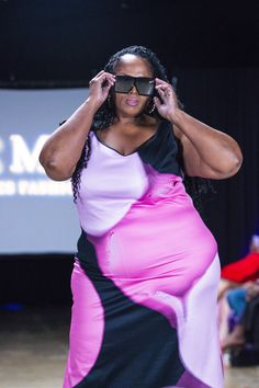 a woman in a pink and black dress is on the runway with her hands behind her head