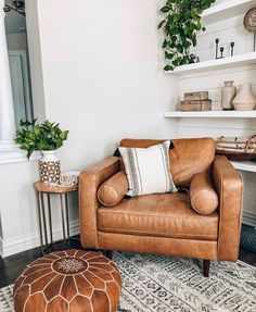 a brown leather chair sitting on top of a rug next to a wooden table and white shelves