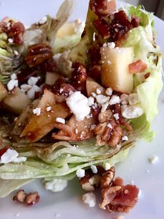 lettuce with apples, walnuts and feta cheese on it sitting on a white plate