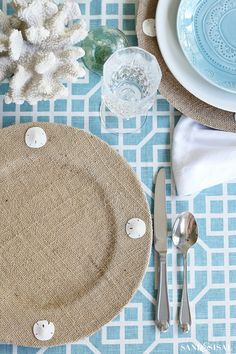 a place setting with plates, silverware and napkins on a blue patterned tablecloth