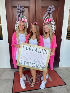 three girls standing in front of a door holding a sign