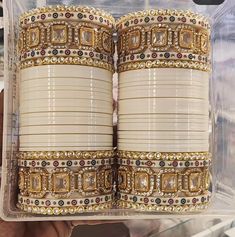 two white bracelets with gold and diamonds on them in a plastic case at a store