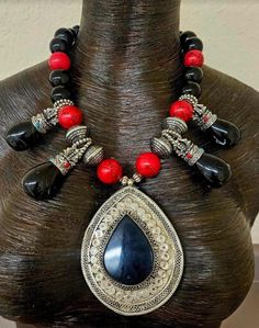 A vintage black onyx and silver tone metal ethnic pendant is featured in this black, red and silver unisex tribal statement necklace.  The primary pendant measures 4" x 3" while the black onyx or black agate teardrops measure 2.5" x 1".  Each teardrop has inlaid turquoise and coral.  The remainder of the necklace includes red magnesite, silver tone tribal bi-cones, silver tone daisy spacers, black onyx beads, black faceted crystals, purple jade and silver tone metal spacers.  Adjusts from 20-23" and closes with silver tone hardware, a lobster claw clasp and a 3" extender chain.  From the Atelier of Kat Kouture! Black Bohemian Jewelry With Polished Beads, Unique Black Teardrop Jewelry, Vintage Black Jewelry With Natural Stones, Traditional Black Necklaces With Large Pendant, Vintage Black Necklaces With Natural Stones, Traditional Black Necklace With Large Pendant, Vintage Black Necklace With Oxidized Finish, Black Teardrop Bohemian Jewelry, Traditional Black Onyx Necklace