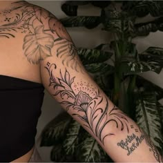 a woman's arm with flowers and words tattooed on her left arm, in front of a potted plant