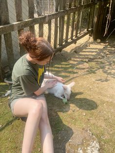 a woman is petting a small white dog on the grass in front of a fence