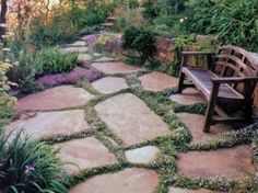 a wooden bench sitting on top of a stone walkway surrounded by flowers and greenery