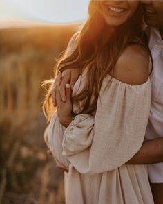 a man and woman hugging each other in an open field at sunset with the sun shining on them