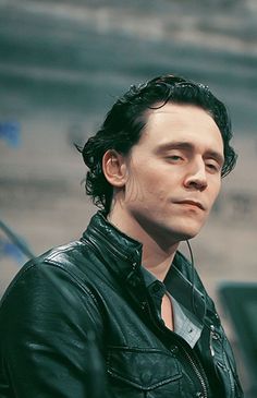 a man in a black leather jacket looking off into the distance with his eyes closed