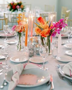 the table is set with plates, silverware and colorful flowers in glass vases