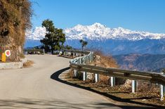 an empty road in the mountains with snow capped mountains in the backgrouds