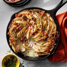 a skillet filled with potatoes and bacon on top of a white table next to bowls of sauces